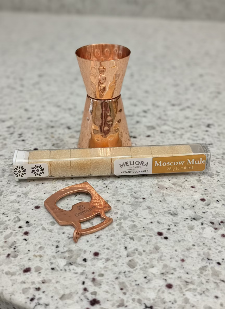 Copper jigger, bottle opener, and Moscow Mule kit on a dark surface