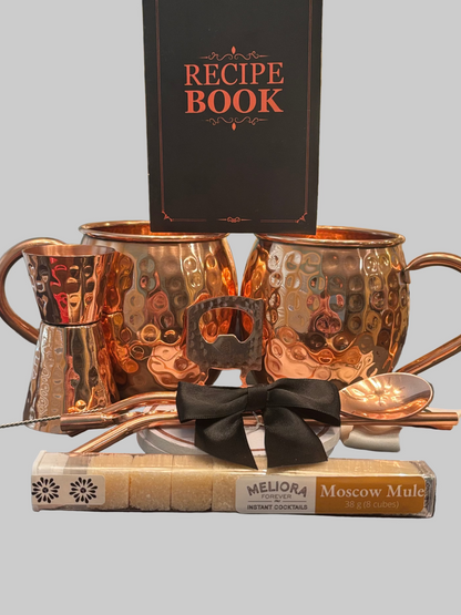 Set of copper mugs with a bottle opener, spoon, and recipe book on a gray background