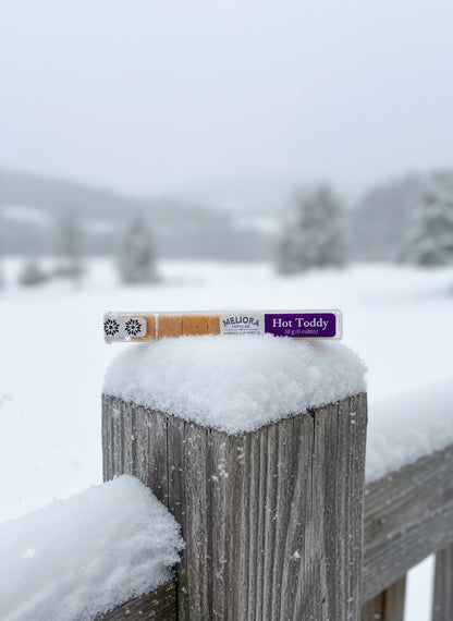 'Hot Toddy'  Instant Cocktail Cubes on a snow-covered wooden post with a snowy landscape in the background.