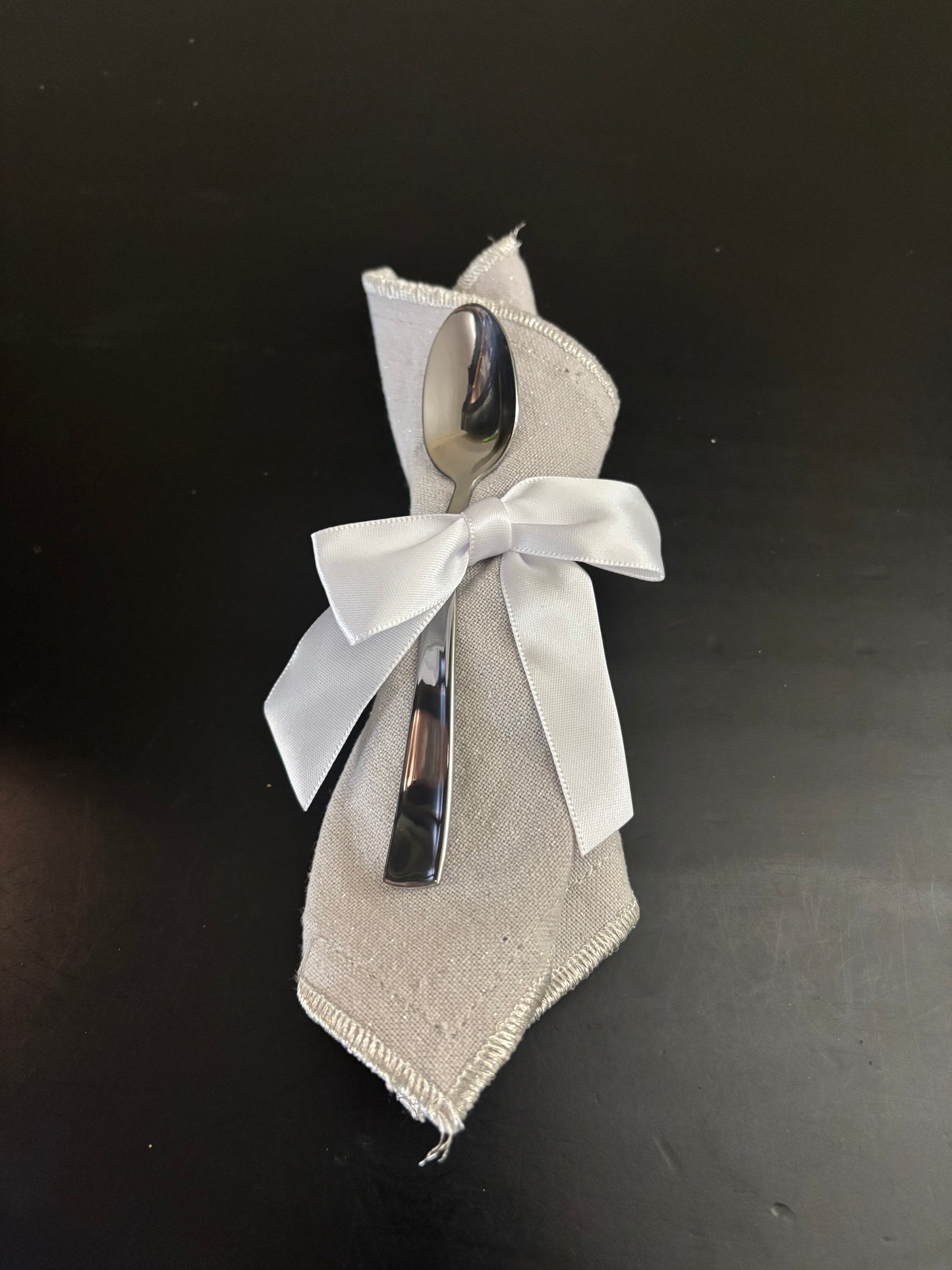 Two silver spoons on beige fabric with a white bow against a black background