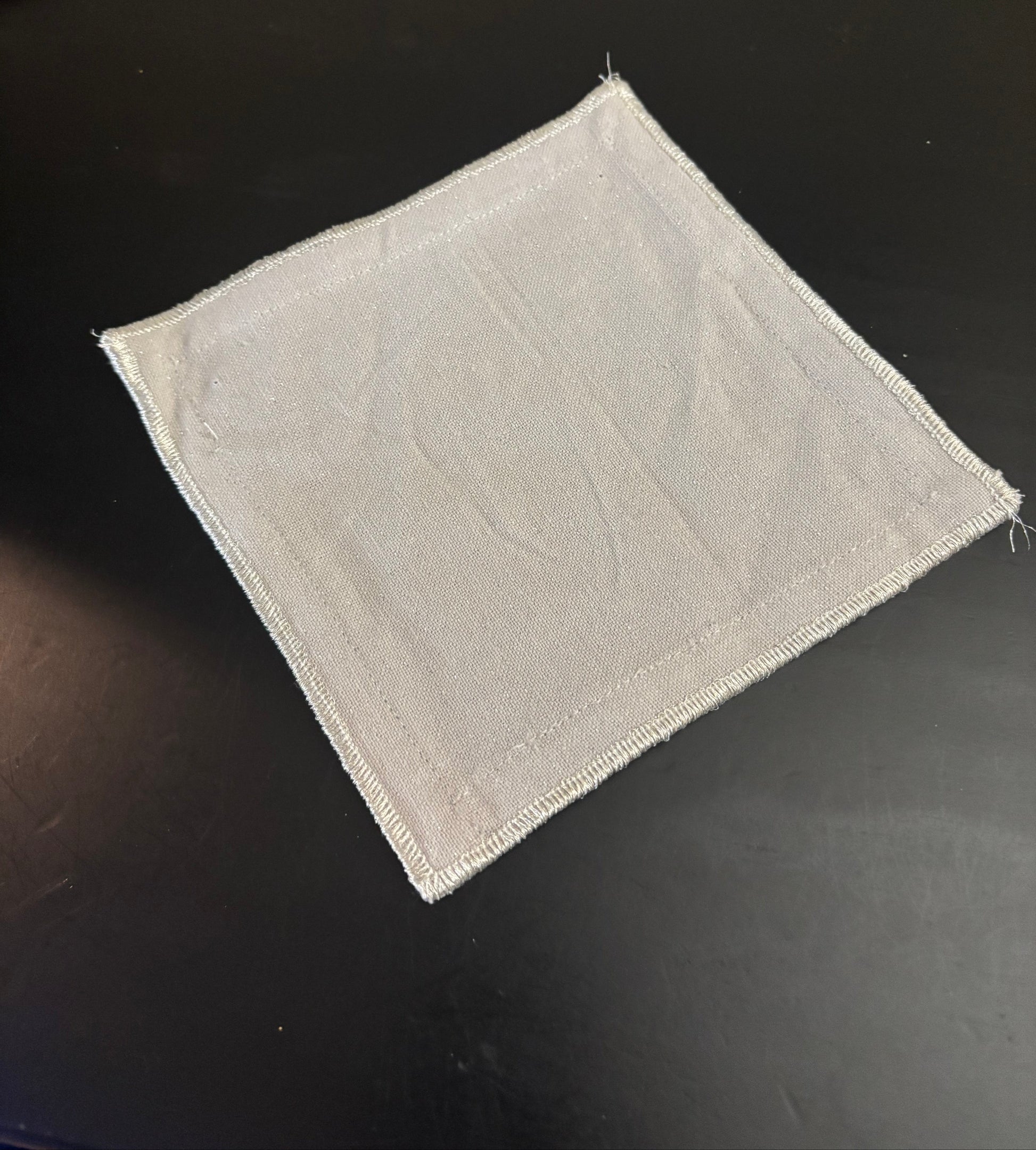 Cocktail Napkin Square piece of light gray fabric on a black background
