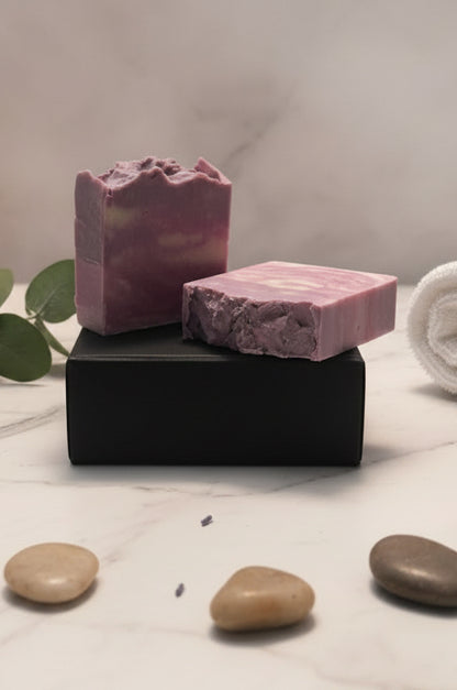 Two purple and pink swirled soap bars on a white surface with a black stand.
