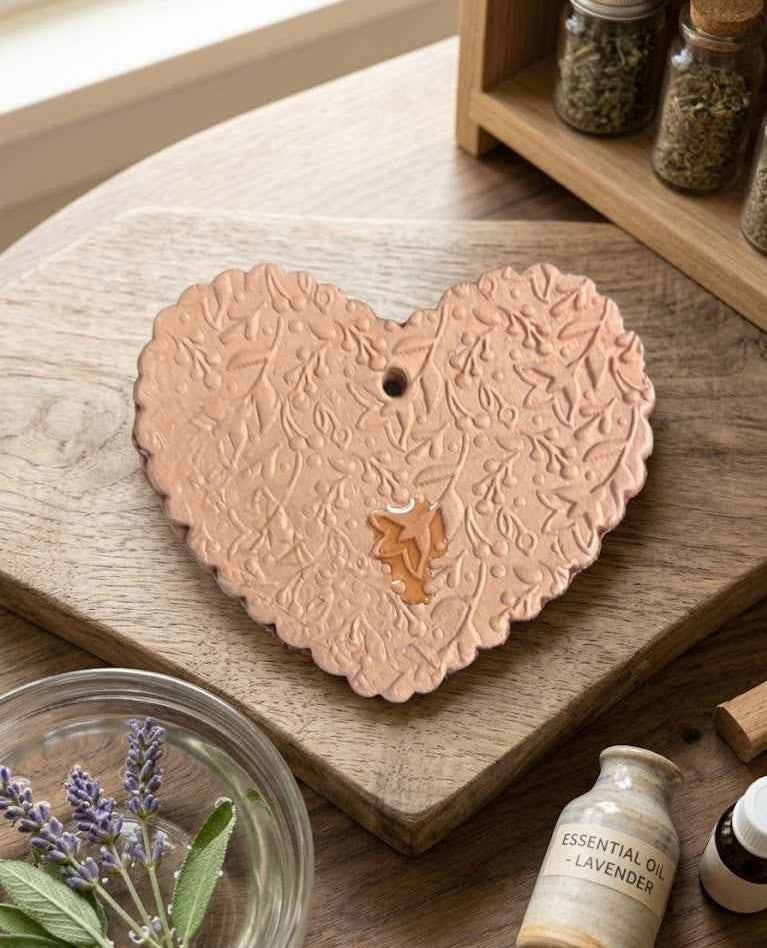 Heart-shaped ceramic incense burner on a wooden surface with lavender and essential oil bottles.
