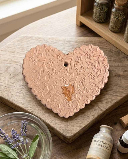 Heart-shaped ceramic incense burner on a wooden surface with lavender and essential oil bottles.